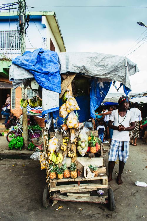 Free Bustling street market with a fruit cart and vendor showcasing fresh produce under blue tarp. Stock Photo