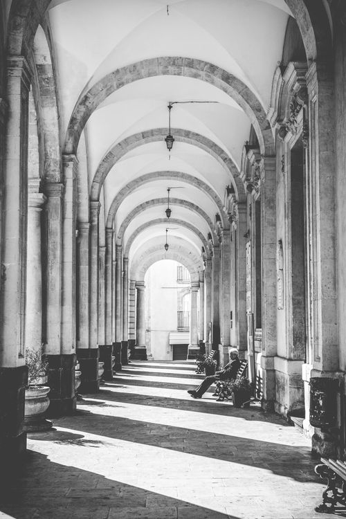 Free Grayscale image of a historical archway with benches and shadow play Stock Photo