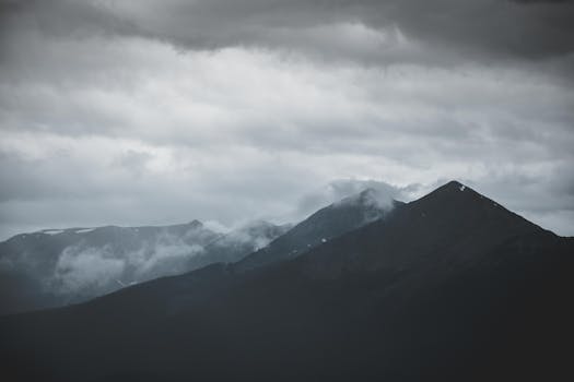 A moody mountain landscape shrouded in clouds and mist creating a dramatic atmosphere.