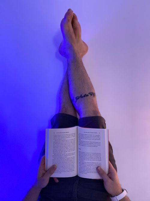 Free Person reading a book while barefoot, showcasing a tattoo under blue light. Stock Photo