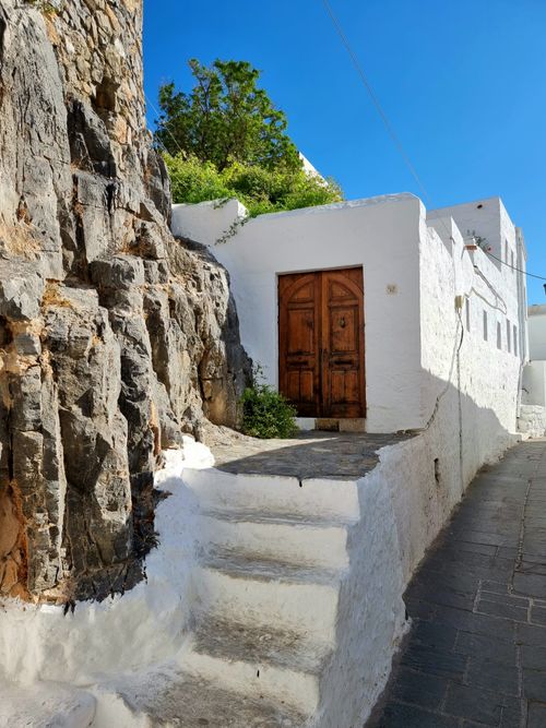Free A picturesque white building with a wooden door and stone steps in the sunny streets of Rhodes, Greece. Stock Photo