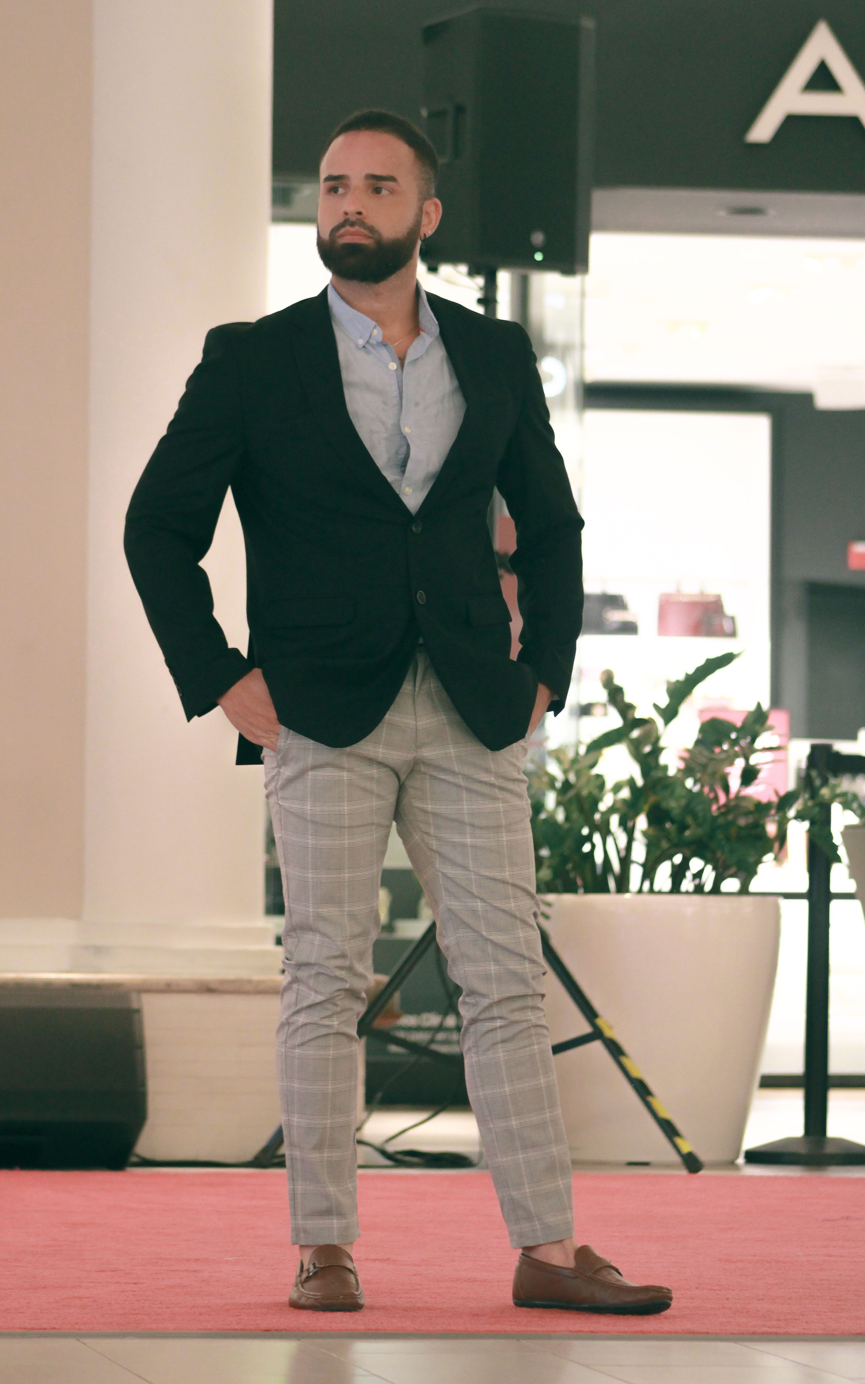 Confident man in stylish attire poses inside a mall setting, exuding elegance.