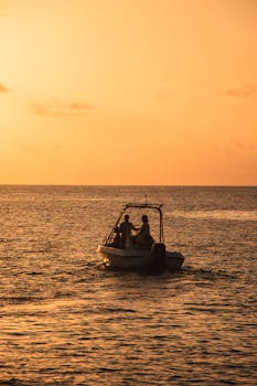 Silhouette of a boat with people enjoying a peaceful sunset on the ocean, casting a warm glow.