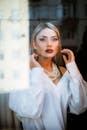 Woman in White Long Sleeves Dress Standing Behind Glass Wall while Posing at the Camera