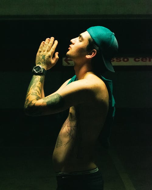 Side View of a Shirtles, Tattooed Man Standing with His Hands in Praying Position 