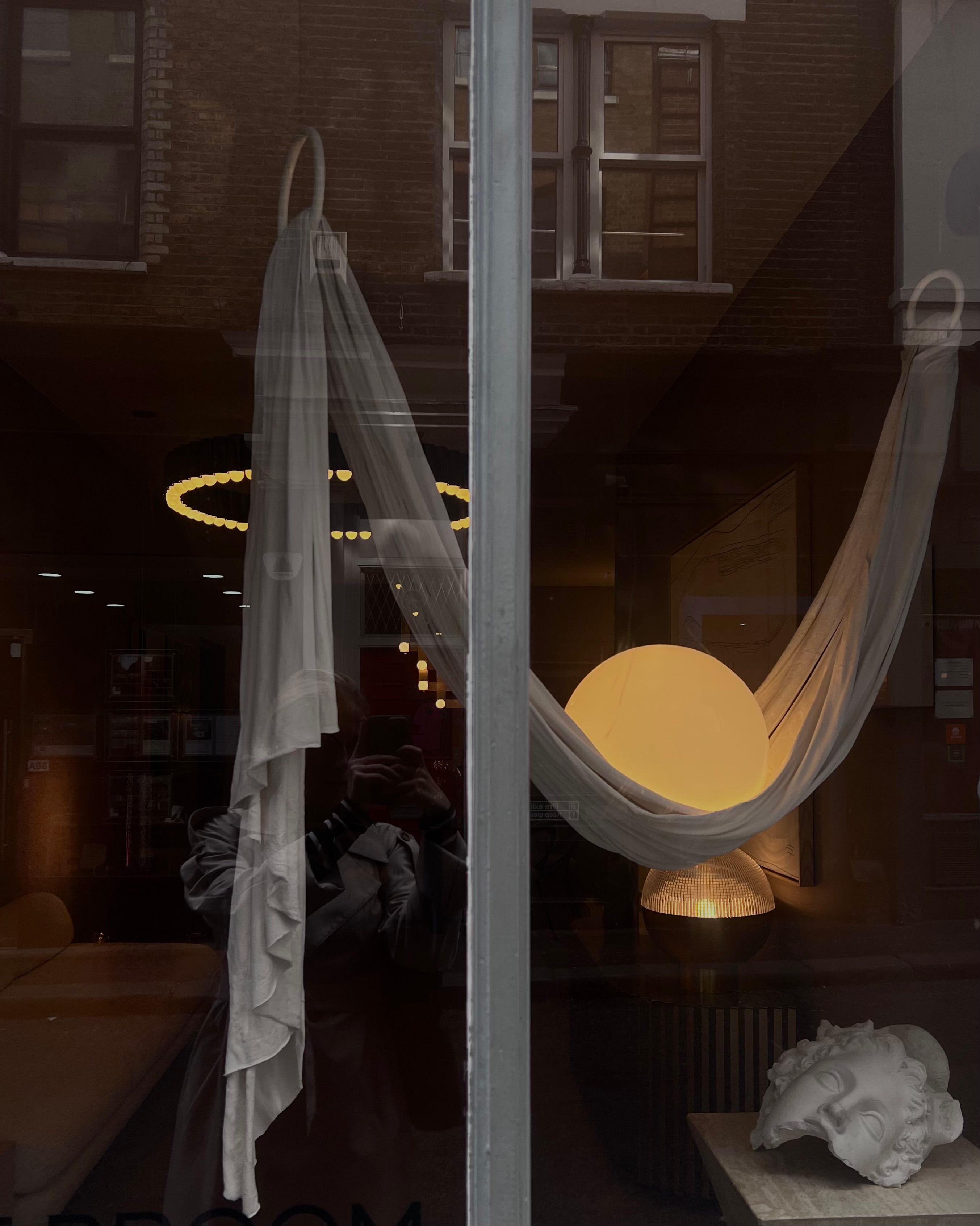 Contemporary art display seen through a window showcases a unique setup with abstract lighting and drapery.