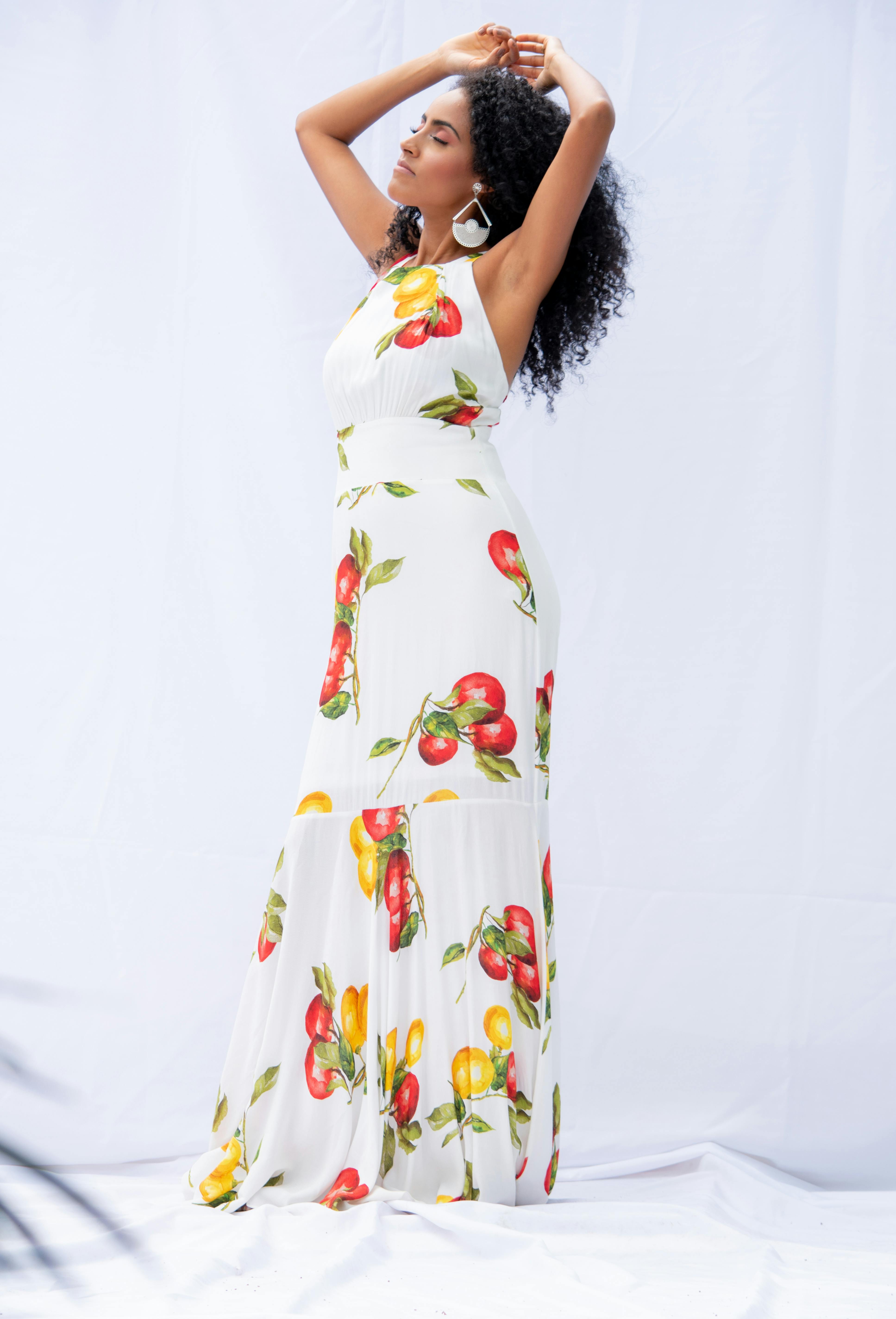 Stylish woman poses elegantly in a fruit-patterned dress in an outdoor photoshoot.