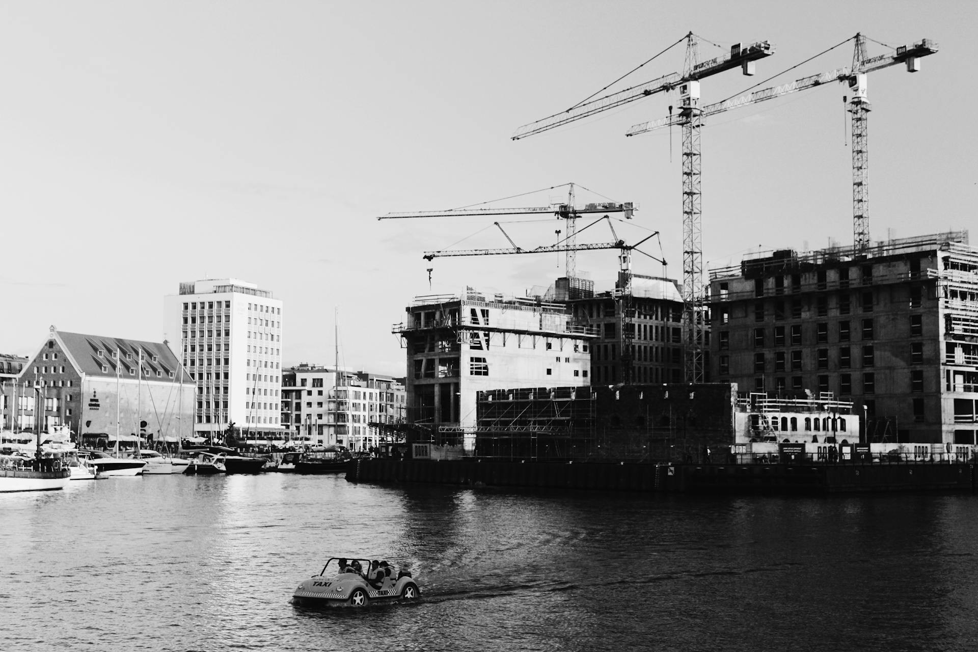 Black and white photo of a waterfront construction site with cranes and boats.