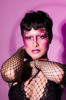 A striking portrait of a woman with bold makeup and stylish fishnet attire against a pink background.