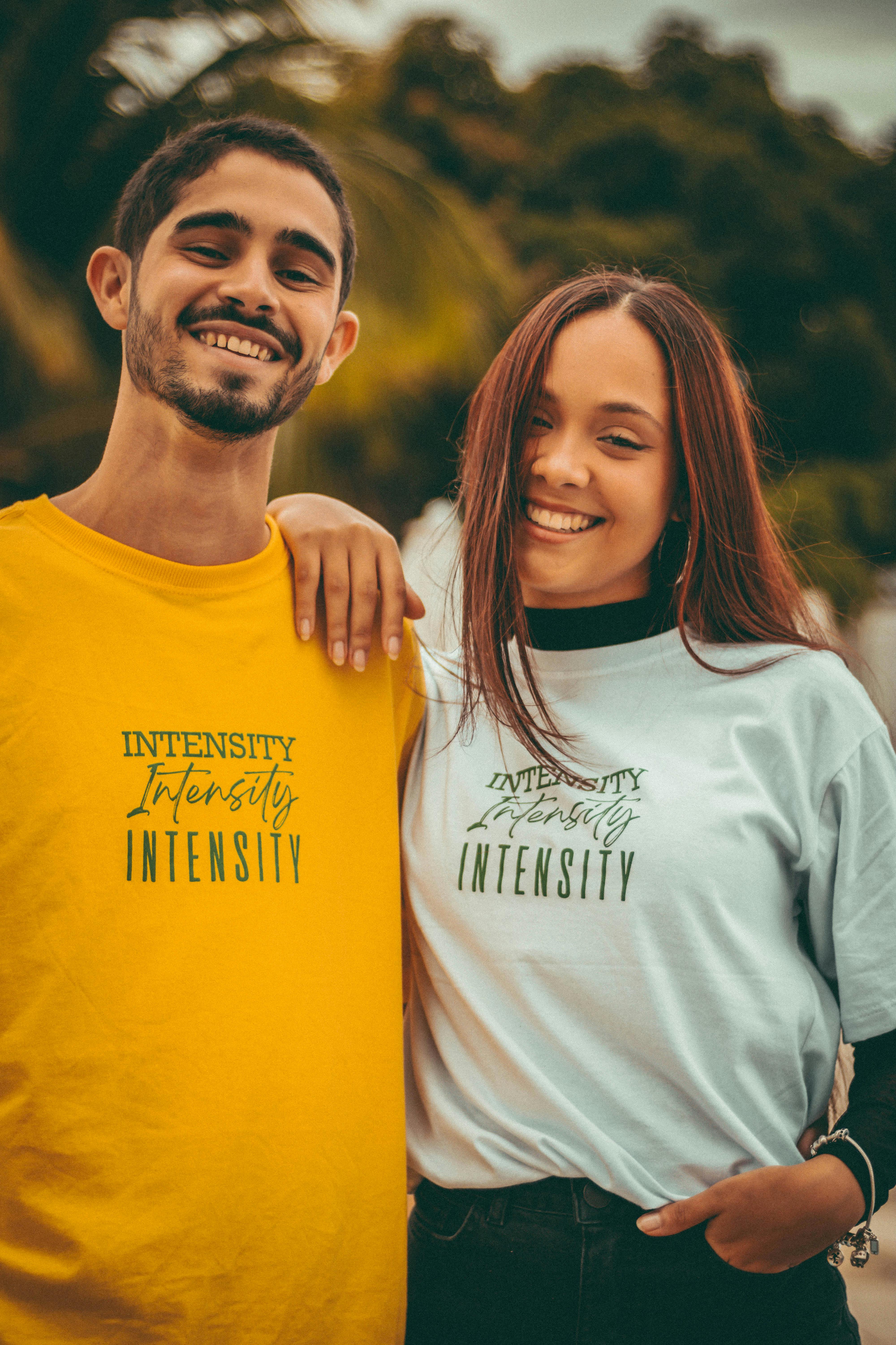 Smiling couple wearing yellow and white shirts with 'Intensity' print enjoying a sunny day outdoors.
