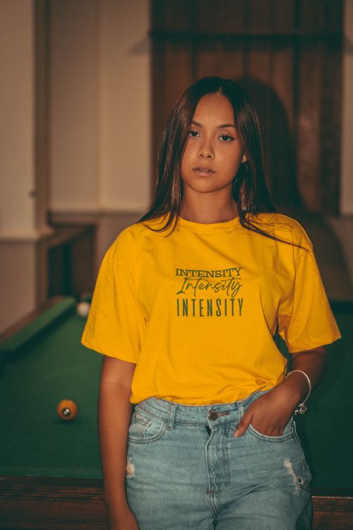 Free Young woman in vibrant yellow t-shirt poses indoors by a billiard table, creating a relaxed yet stylish look. Stock Photo