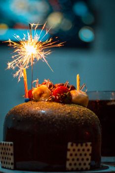 Indulgent chocolate cake with fruit toppings, illuminated by a sparkling candle for celebration.