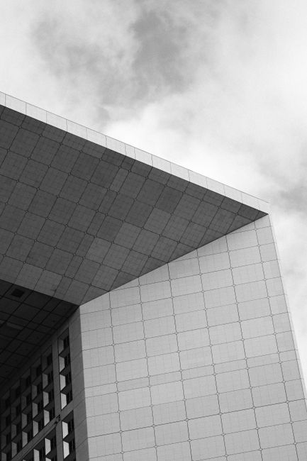 Black and white architectural shot of a modern geometric concrete structure against cloudy sky.