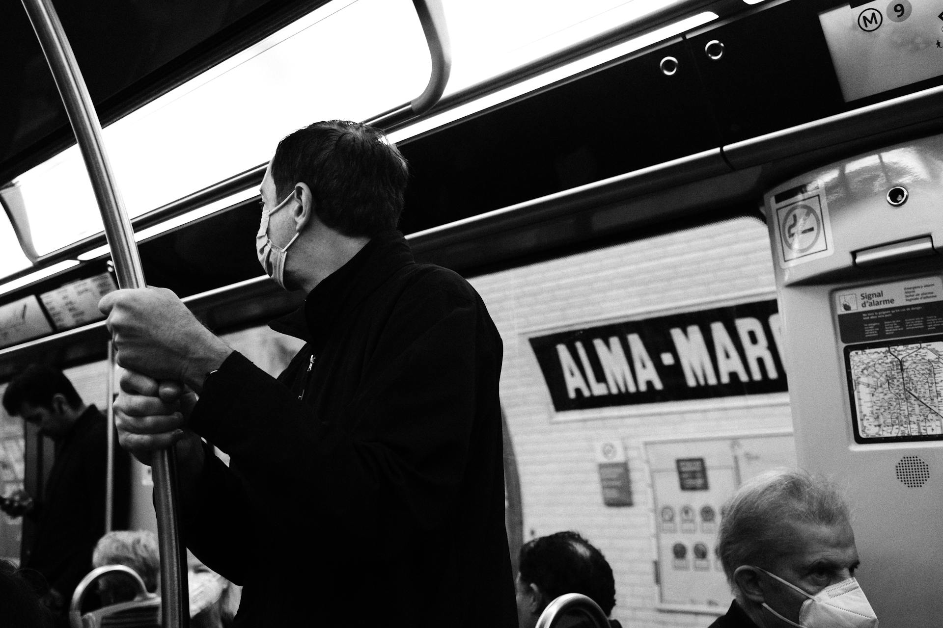 Black and white image of masked commuters on a subway train at Alma-Marceau station.