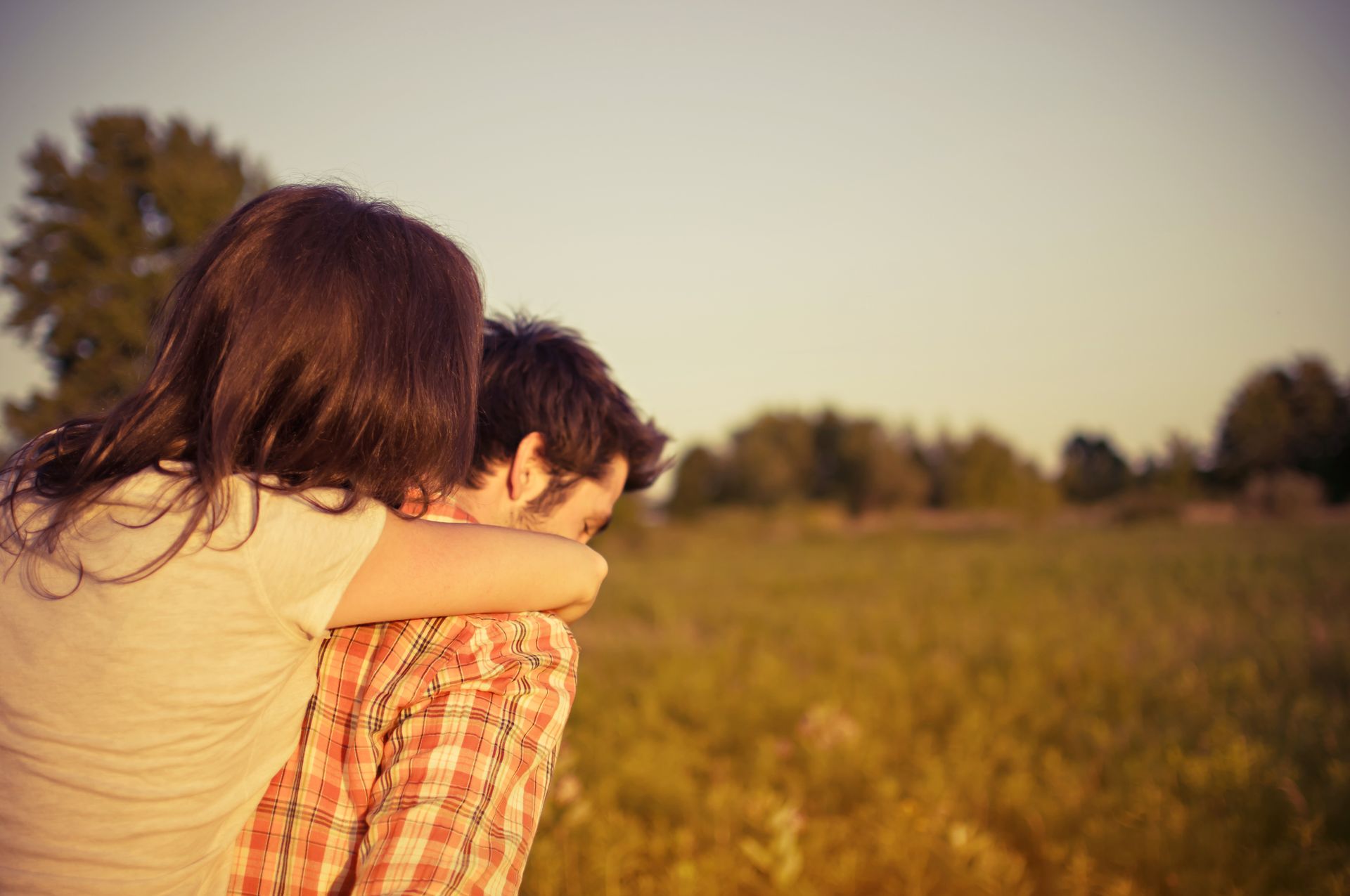 A couple shares a loving embrace during a sunset in a tranquil field.
