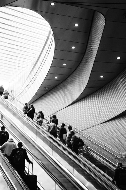 Black and white photo of people on escalators in a modern architecture setting.