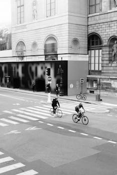 Black and white photo of cyclists crossing a city street with a historic building backdrop.