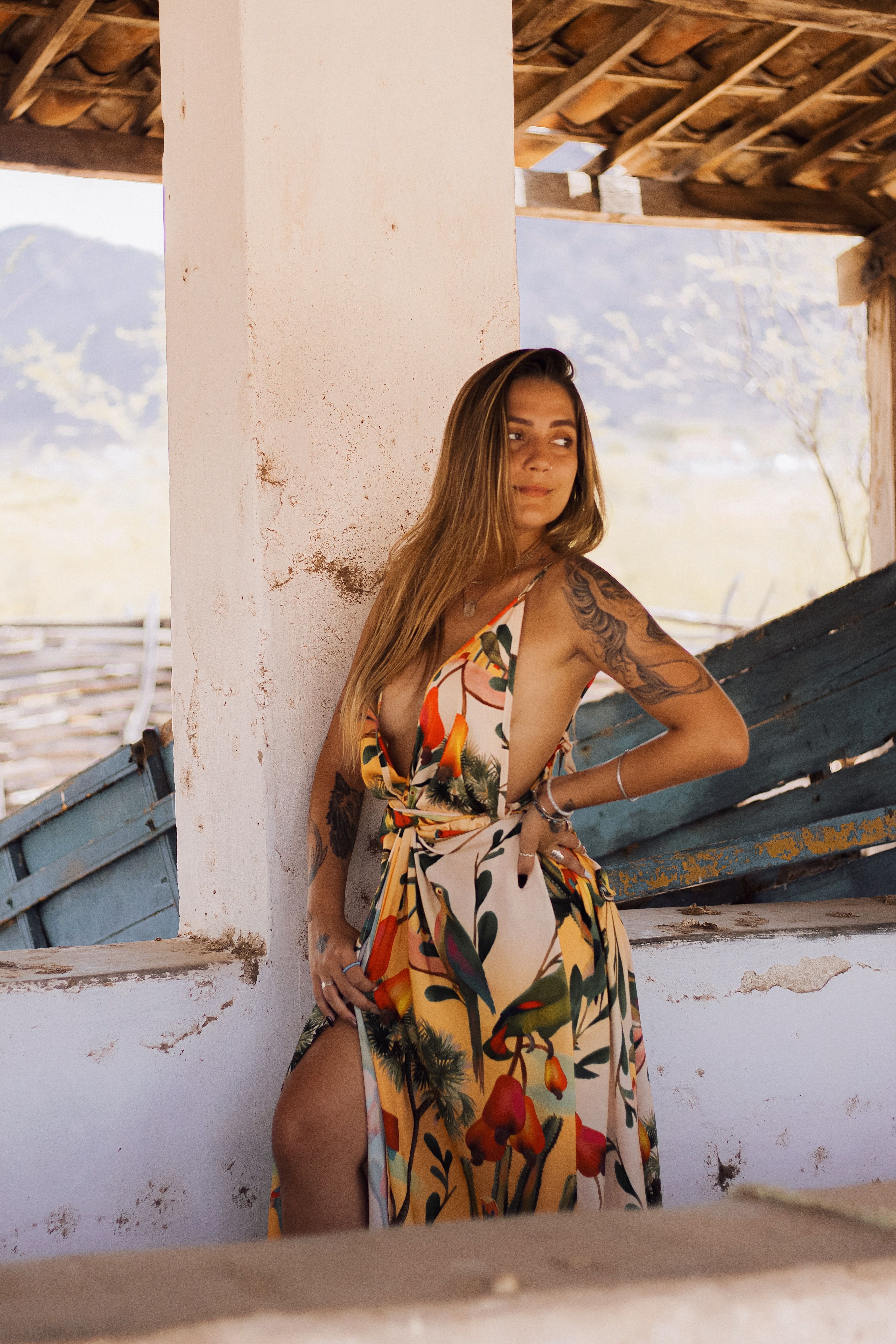 Fashionable woman with tattoos posing in a vibrant floral dress.