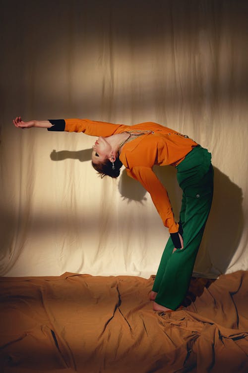 Woman in an Orange Blouse and a Green Pants Stretching Backwards 
