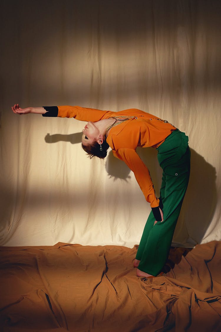 Woman In An Orange Blouse And A Green Pants Stretching Backwards 