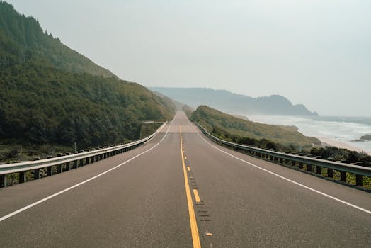 A tranquil view of a straight coastal road flanked by misty mountains and the ocean.