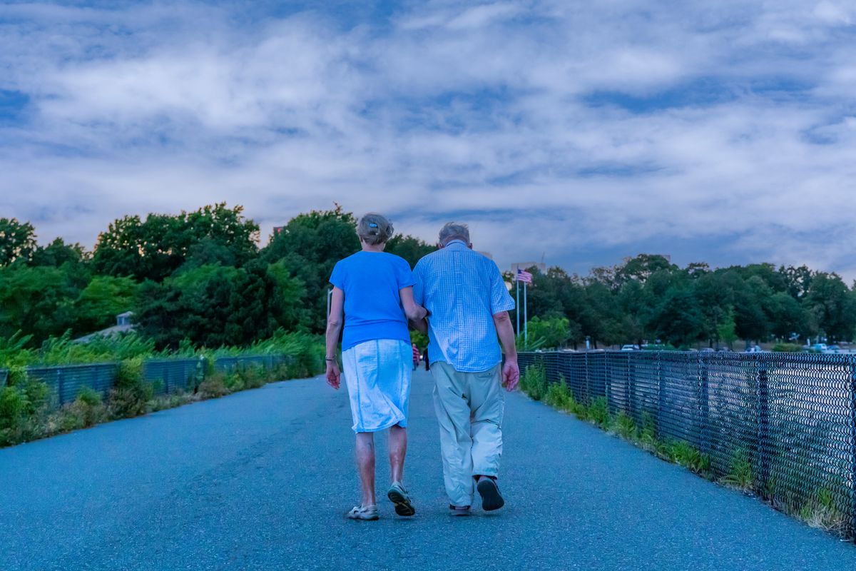 Couple over 55 walking together on an outdoor pathway under a cloudy sky