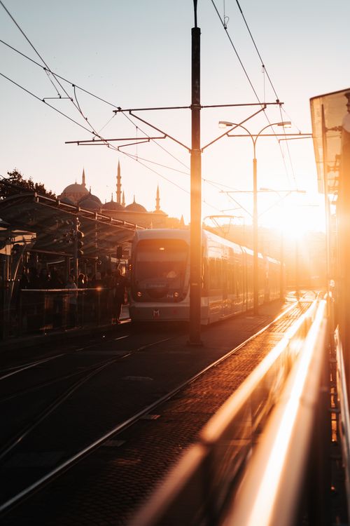 Free Tram arriving at a station during sunset with a cityscape in the background. Stock Photo
