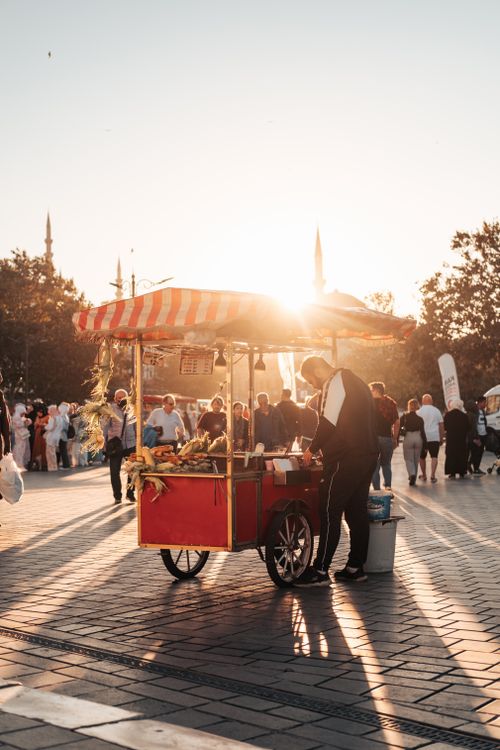 Free Vibrant street scene with a food cart and crowd during sunset in a lively town square. Stock Photo
