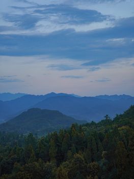 A tranquil mountain landscape with fog and forest at dusk, creating a serene atmosphere.