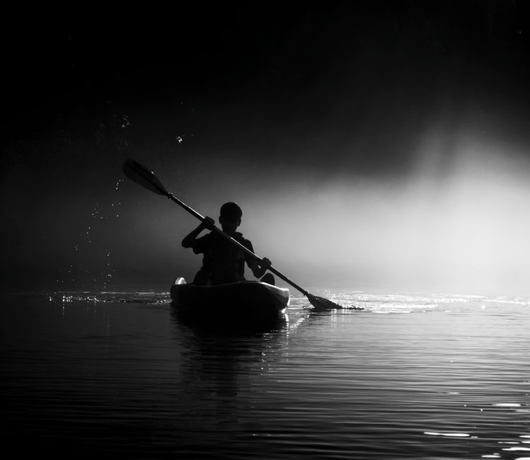 A kayaker paddling through misty water at dawn, the kind of low-light conditions where a waterproof headlamp matters