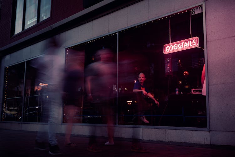 Photo Of People Walking By A Bar 