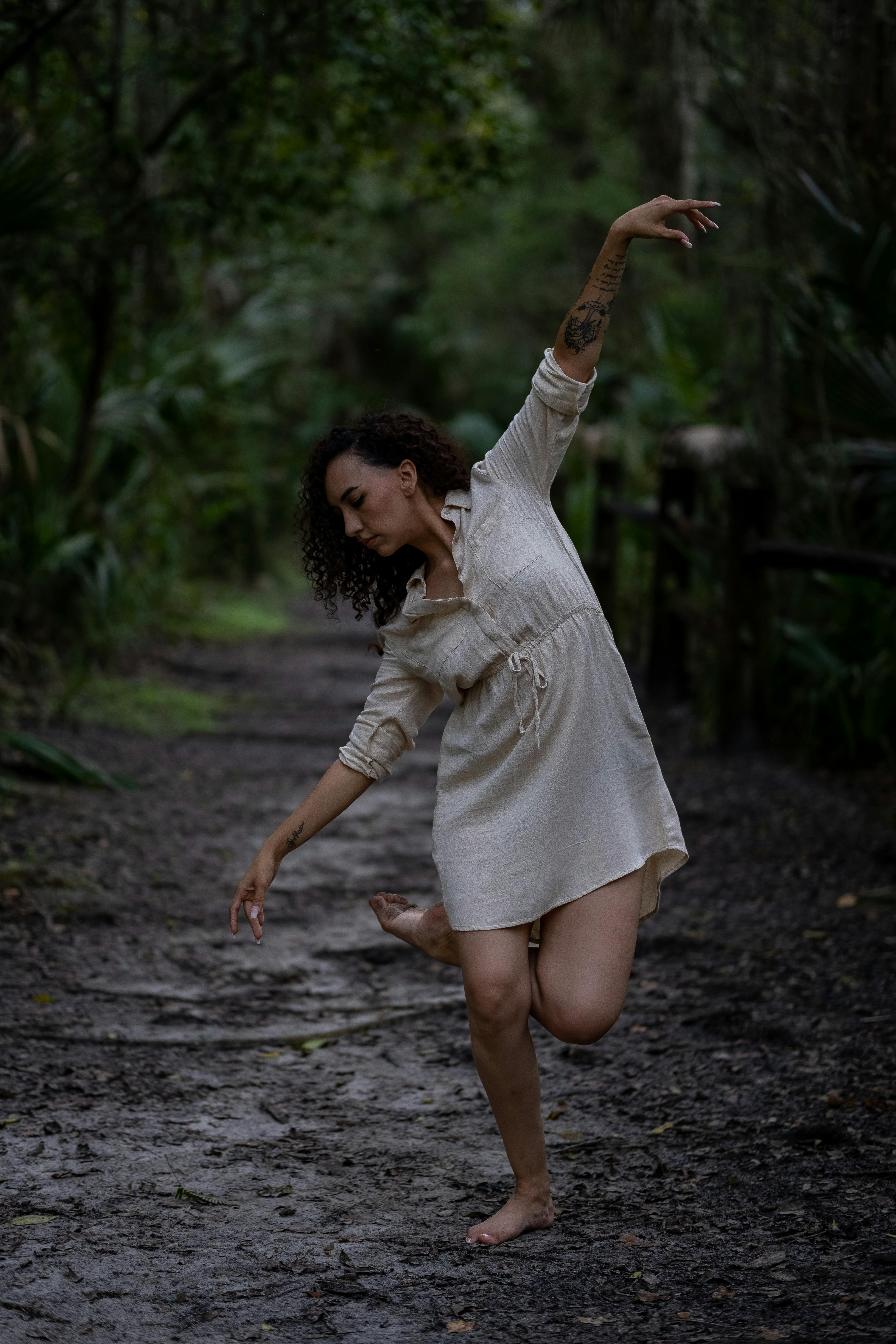 Free Barefoot woman in a beige dress dancing on a forest path with natural elegance. Stock Photo
