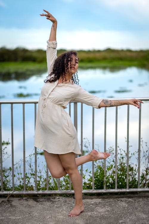 Woman Wearing Beige Dress Dancing Beside a Railing