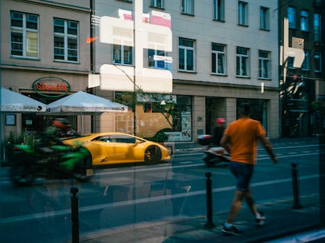 Urban reflection in window showing a luxury yellow car, pedestrians, and buildings.