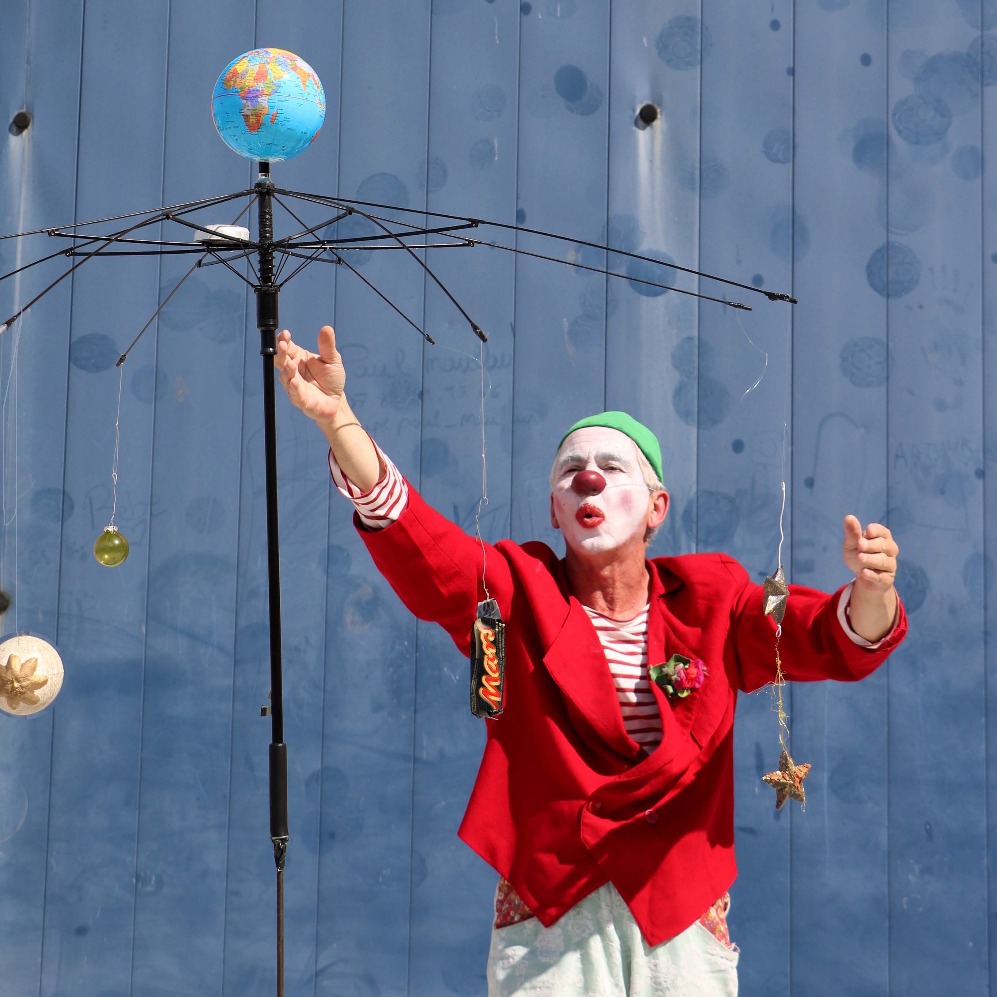 Vibrant clown performing with unique umbrella setup against a blue background.