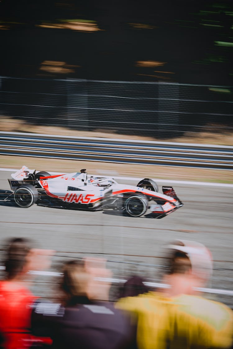 People Watching A Red And White Racing Car On Race Track