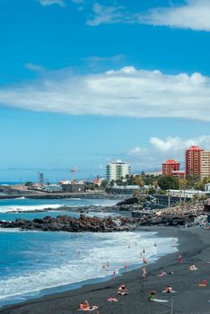 Relaxing day at Puerto de la Cruz's unique black sand beach with cityscape view.