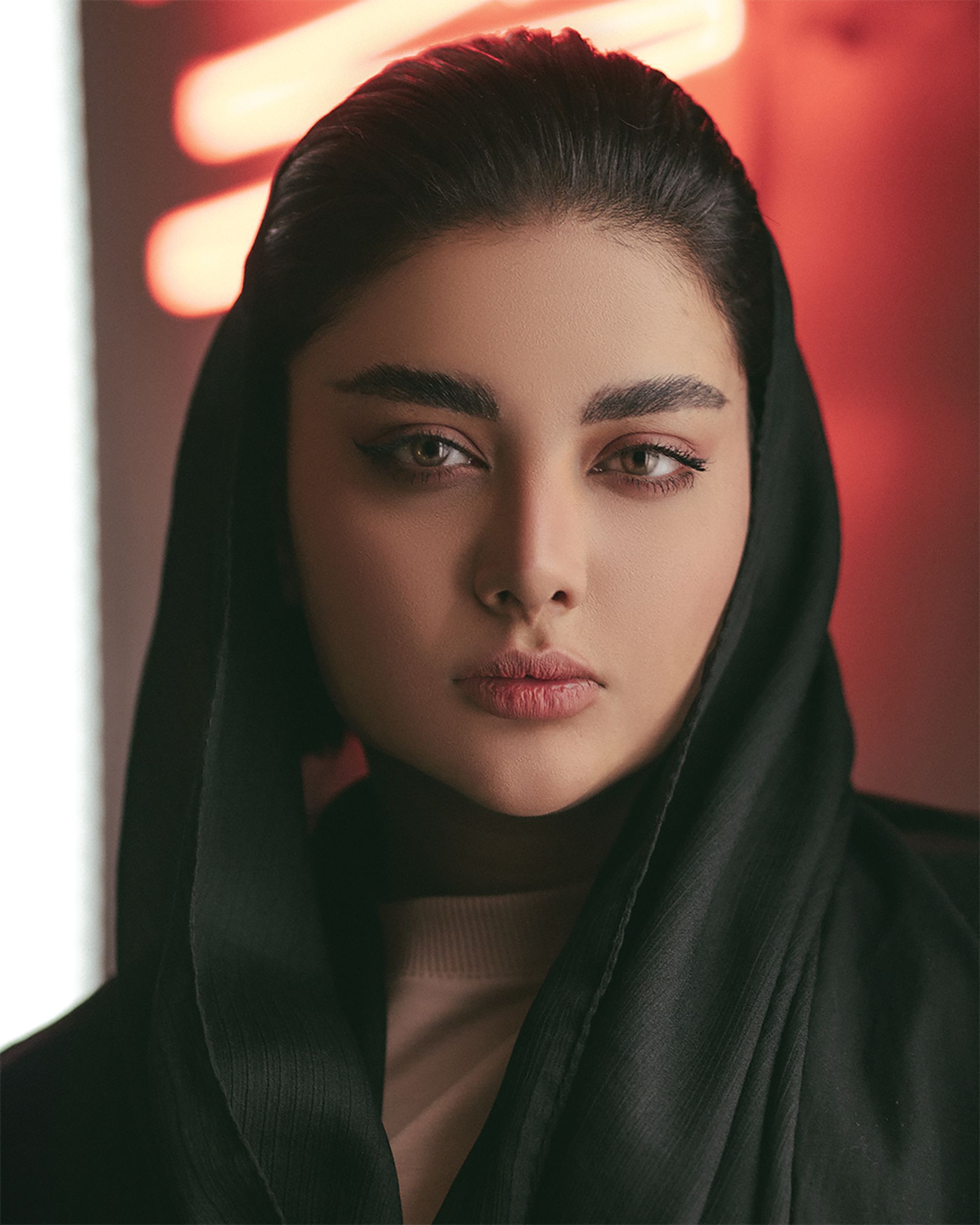 Elegant portrait of a woman wearing a black hijab, with warm background lighting.