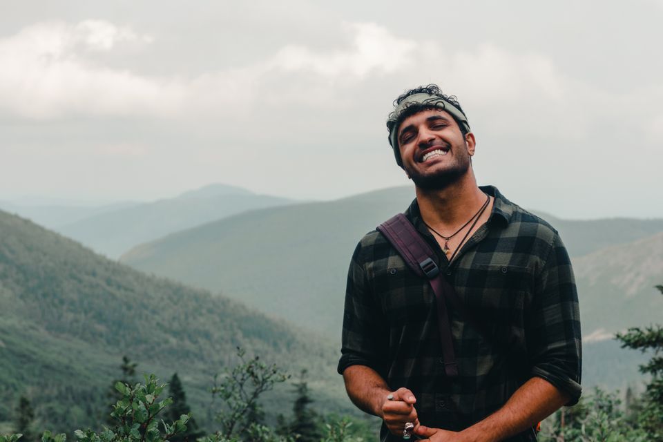 A smiling man in a plaid shirt hiking in the mountains