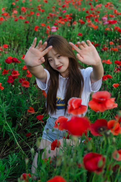 Woman Sitting with Arms Raised among Poppy Flowers