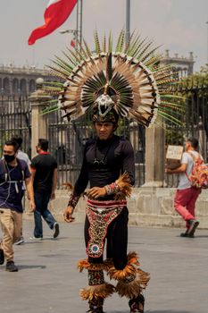 Aztec warrior in a vibrant costume walking in Mexico City's historic streets.