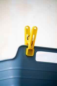Close-up of a yellow clothespin clipped onto the edge of a blue plastic storage box, studio shot.