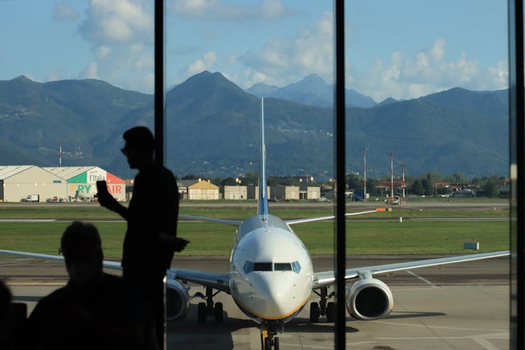 Silhouette Of Person Standing Beside Glass Wall Near Parked Airplane