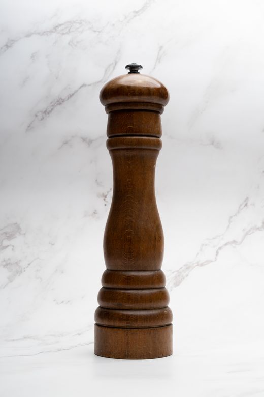 Tall dark wooden pepper mill standing against white marble background
