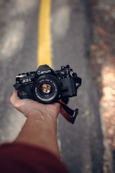 A vintage Canon AE-1 camera is held in a hand with a blurred outdoor background.
