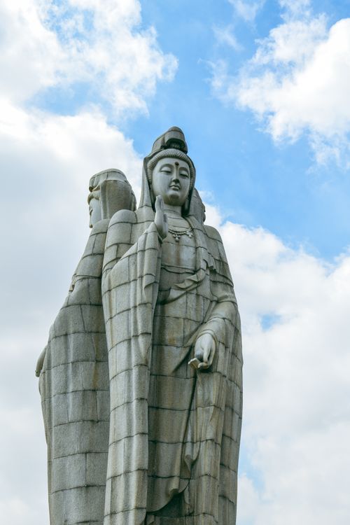 Free Two grand statues of serene figures against a vibrant blue sky symbolize spirituality and calm. Stock Photo