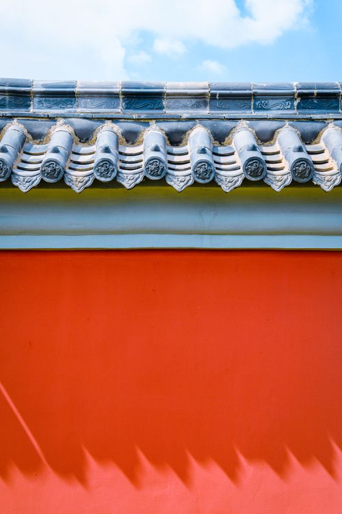 Free Close-up of a vibrant red wall with traditional Chinese tiled roof under a clear sky. Stock Photo