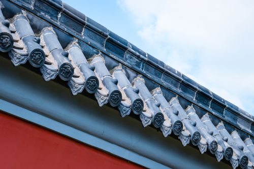 Free Close-up of a traditional Asian rooftop featuring blue tiles and red wall under a clear sky. Stock Photo