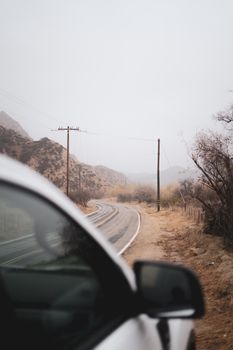 Scenic view of a foggy rural road with a car parked by the roadside and leafless trees.