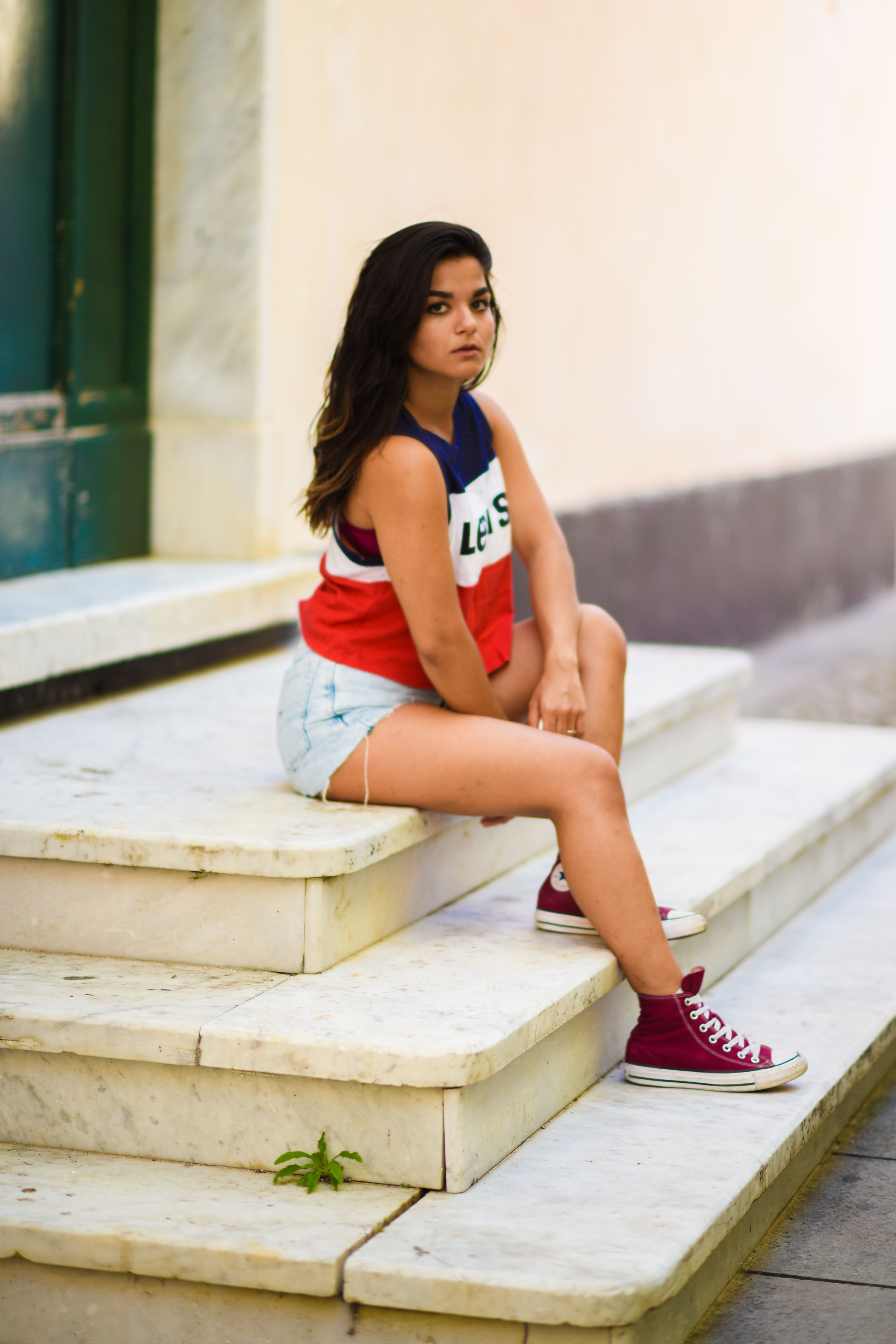 Young woman in casual summer attire sitting on marble steps outdoors.